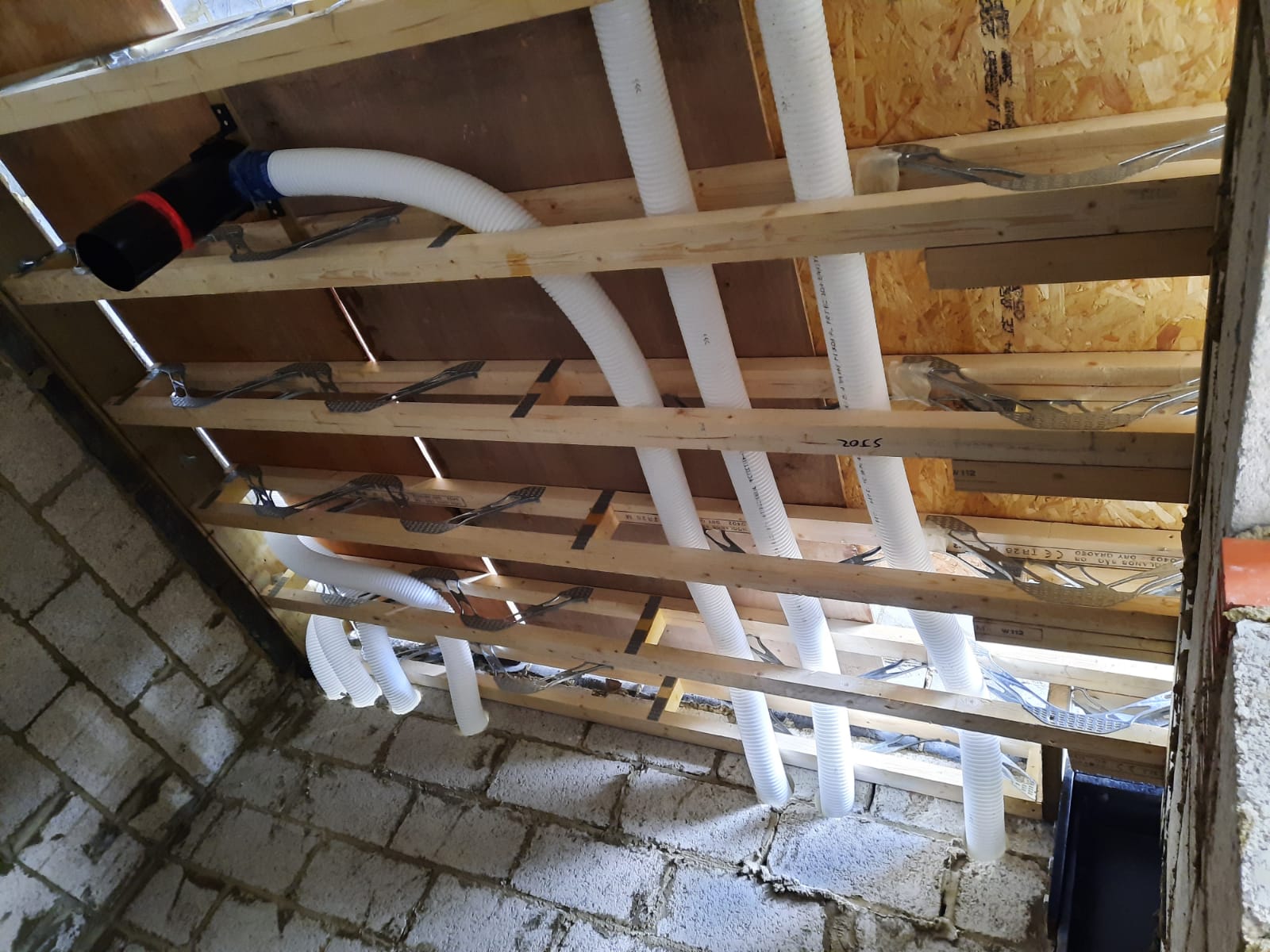 90mm semi-rigid ducting in webbed joists and passing through core-drilled blockwork wall for MVHR system